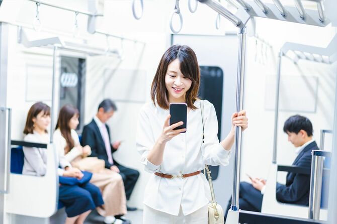 電車の中でスマートフォンを使っている若い女性