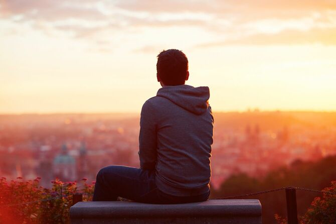 一人で腰を下ろし、見晴らしの良い場所で日の出を見ている男性