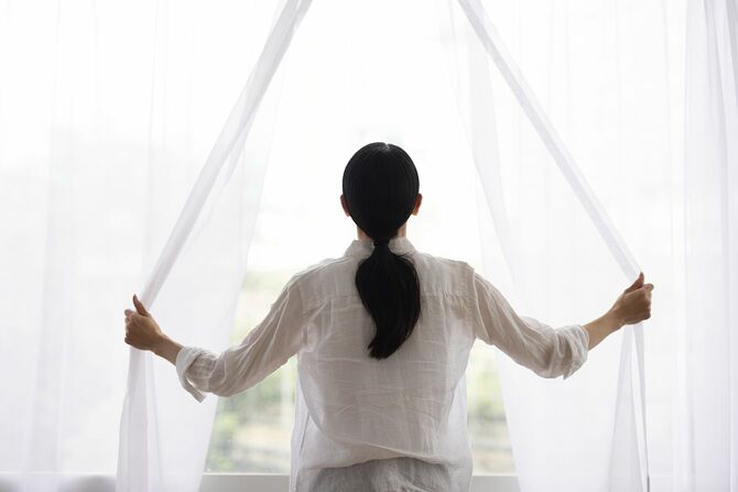 朝の光を入れるためにカーテンを開ける女性