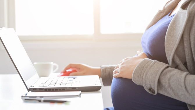 妊婦がノートパソコンとスマホを使って仕事をしている様子