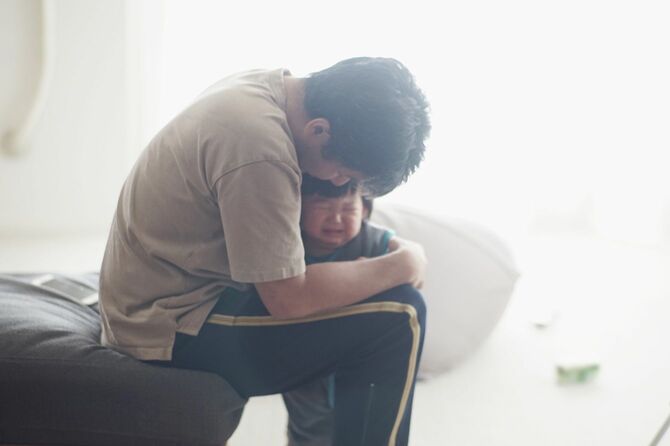 泣いている男の子を家で抱く親