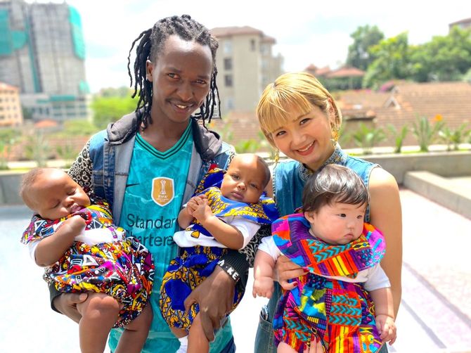 ラハ・ケニアの洋服を着た娘を抱く河野リエさん（右）。隣は創業時から同社に製品を提供するテーラーのウィリアムさんとその子どもたち