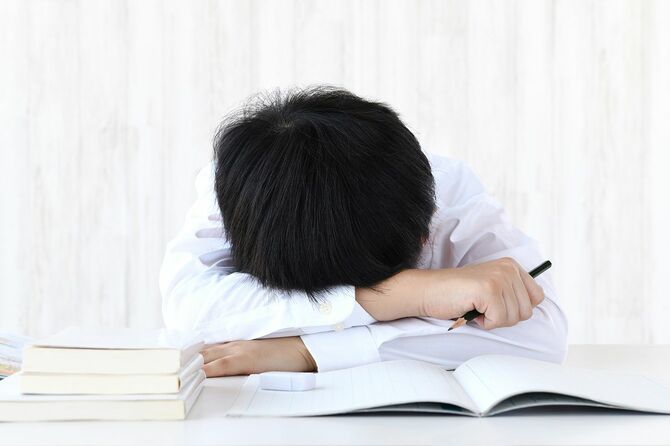 机の上にうつ伏せに横たわっている少年、彼はもう勉強したくない