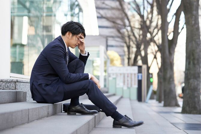 屋外の階段に座り込んでいる悩まし気な男性