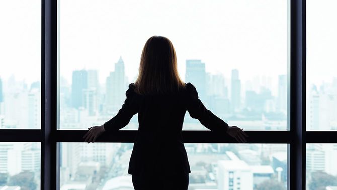 アジアのビジネス女性立って、窓の外を見て都市ビューの背景