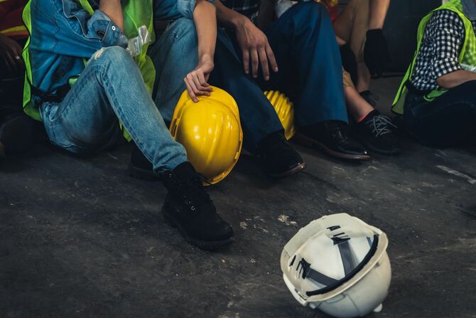 床に座り込み、ヘルメットを脱いで休んでいる作業員たち