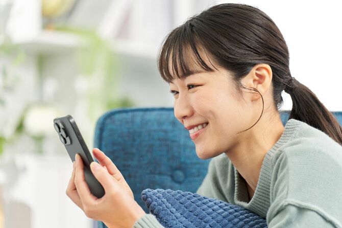 ソファに横になってスマートフォンを見ている女性
