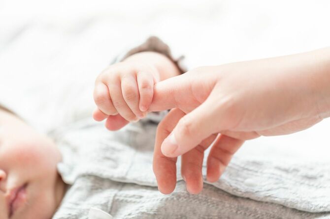 明るい部屋で、母親の人差し指を握る赤ん坊