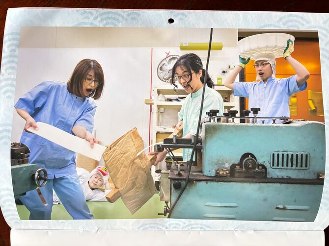 フォトグラファー・浅田政志さん撮影の写真で作った、野田米菓の2024年カレンダー。日常の一コマのようなシーンの後ろに、寝転んだ恵子さんがいるシュールな一枚