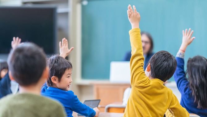 小学校の教室で、一斉に手を挙げる子どもたち