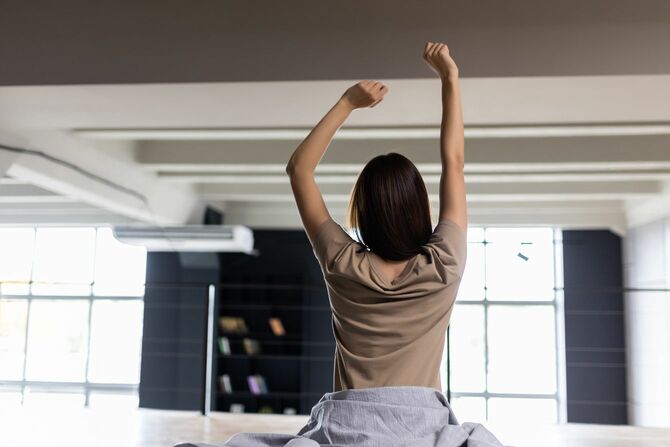 目覚めた後にベッドで伸びる若い女性