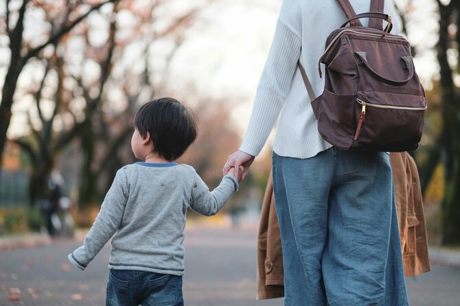 小さな息子と手をつないで公園を歩く母親