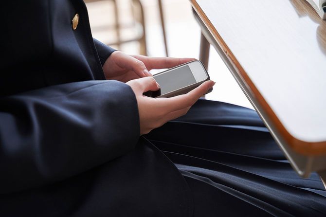 学校の教室の席でスマホを使用する女子学生