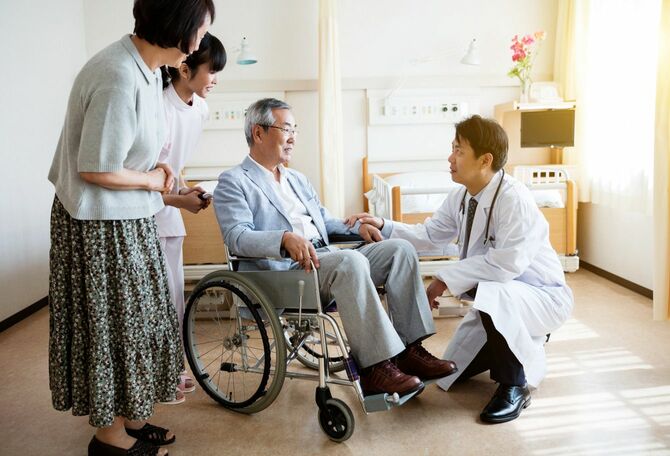 車椅子に座っているシニア男性と医師、付き添いの家族