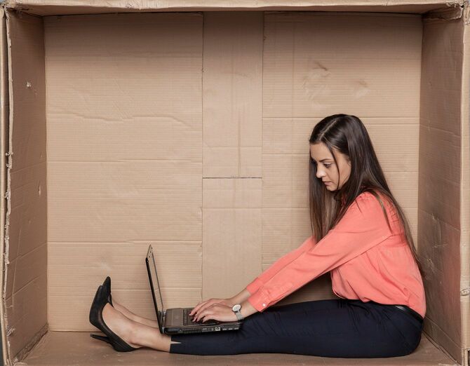 段ボールで囲われた狭い場所でパソコンを使用する女性