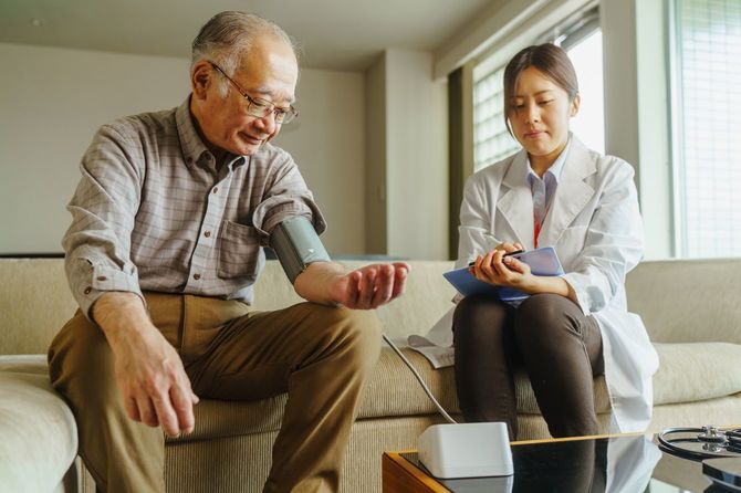 シニア男性患者を訪問し、血圧を測定する医師