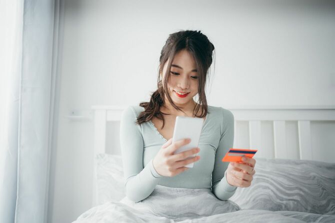 ベッドでスマートフォンを操作する女性